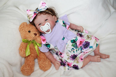 A baby doll wearing a purple dress and a decorative flower headband.